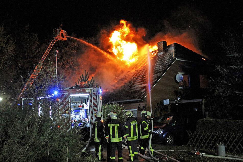 Feuerwehrleute löschen unter anderem von einer Drehleiter aus das brennende Wohnhaus.