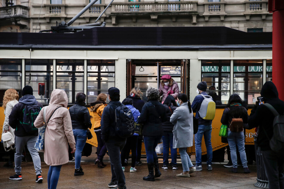 Menschen warten in Mailand, bis sie in die stehende Straßenbahn einsteigen können. Italienische Gesundheitsbehörden erklärten, das Land sei in einer "akuten Phase", nachdem die Fälle der Corona-Infektionen wieder besorgniserregend steigen.