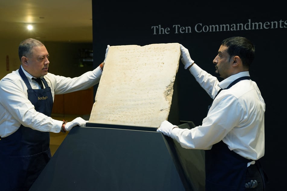 Sotheby’s workers hold one of the most widely known and influential texts in history: the oldest inscribed stone tablet of the Ten Commandments during a press preview at Sotheby’s in New York, on December 9, 2024.