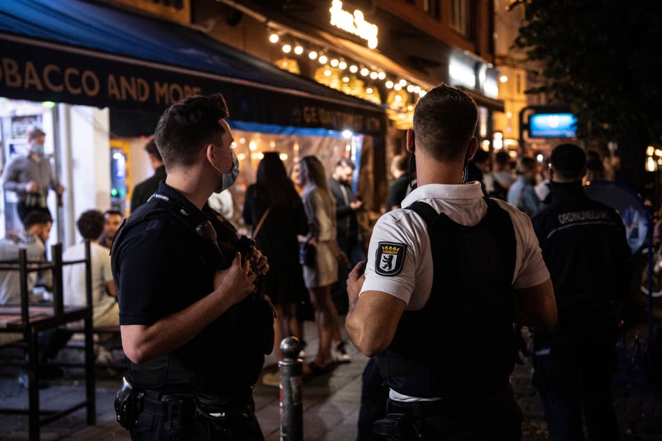 Ein Polizeibeamter und ein Mitarbeiter des Ordnungsamtes stehen vor einem Lokal.