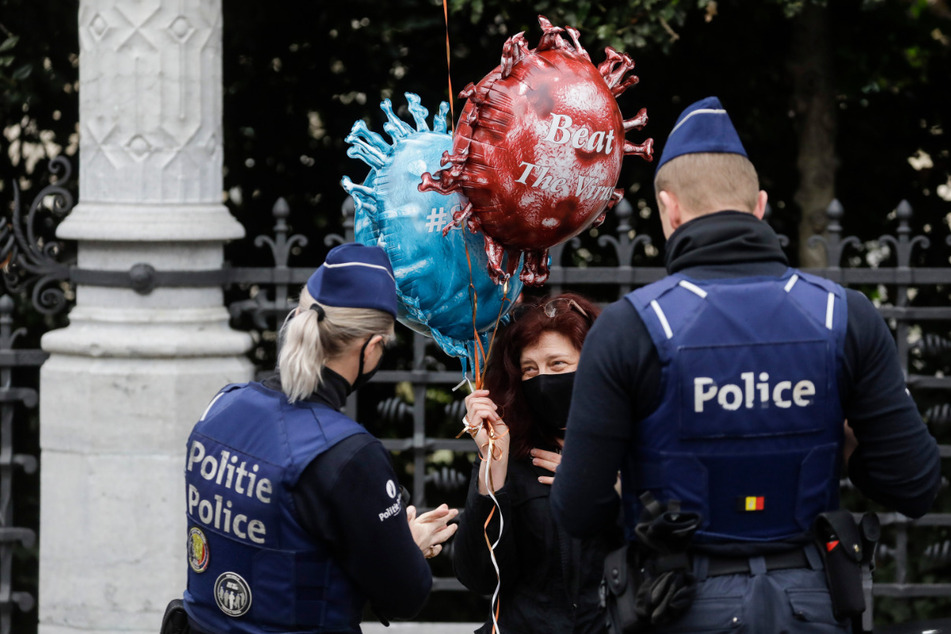 Zwei Polizeibeamte sprechen in Brüssel mit einer Frau (M), die Luftballons in Form eines Virus mit der Aufschrift "Beat The Virus" ("Bekämpft den Virus") hält.