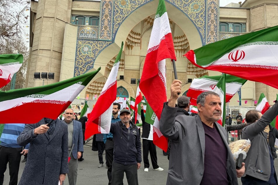 Eine Gruppe von Männern schwenkt iranische Fahnen, während sie an einer Demonstration zur Unterstützung der Regierung und gegen US-amerikanische und israelische Angriffe teilnehmen.