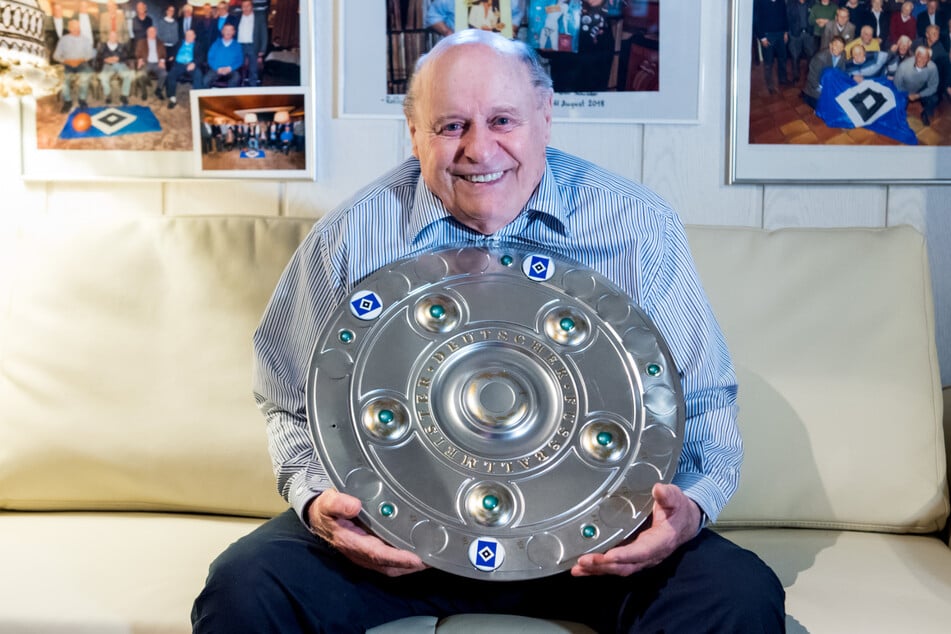 HSV-Legende Gert "Charly" Dörfel (85) sitzt mit einer Kopie der Meisterschale auf dem Sofa. 1960 holte er mit den Rothosen die deutsche Meisterschaft. (Archivfoto)