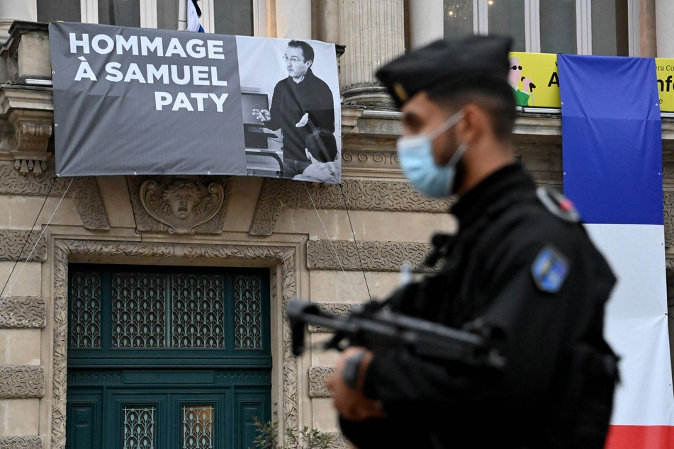 Ein Polizist steht neben der Opera Comedie, an deren Fassade eine Hommage an den enthaupteten Lehrer Samuel Paty angebracht ist.