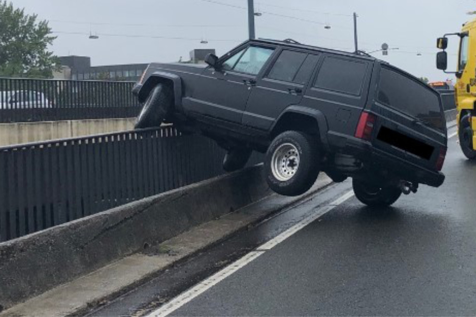 Jeep hängt schief auf Brückengeländer, direkt dahinter lauert der Abgrund