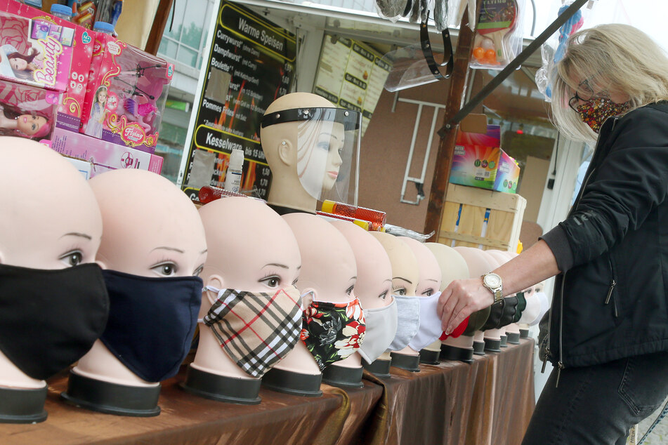 Eine Frau mit Mund-Nasen-Schutz betrachtet auf einem Wochenmarkt handgefertigte Schutzmasken, die zum Kauf angeboten werden. (Archivbild)