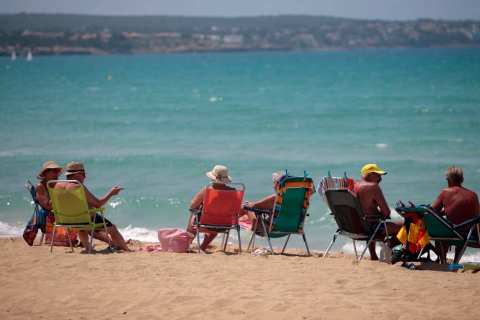 Badegäste sitzen am Strand von Palma de Mallorca. Nach wochenlanger Corona-Pause ist am Montagvormittag erstmals wieder eine Maschine mit Urlaubern aus Deutschland in Mallorca gelandet.