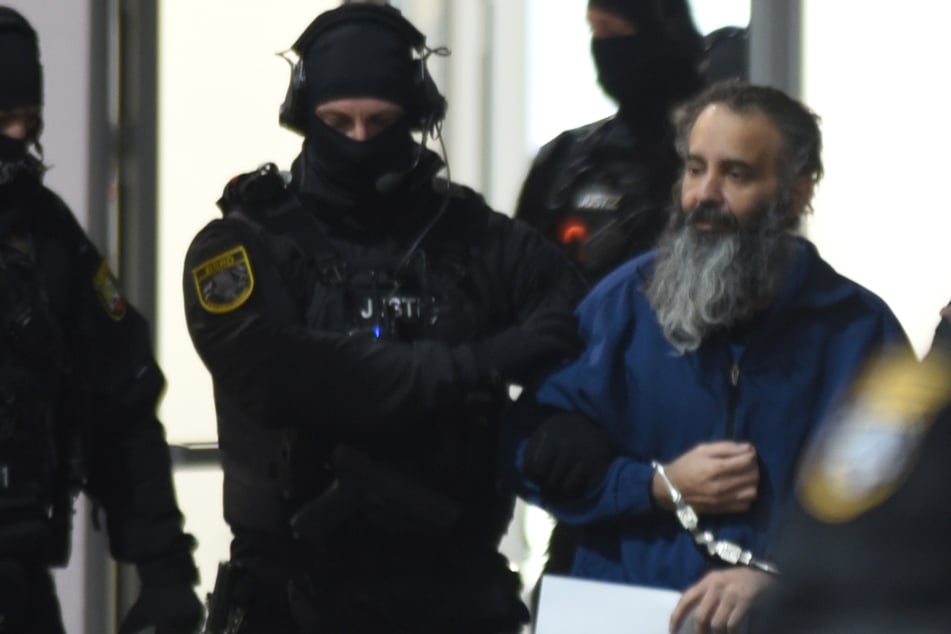 Taleb A. (51) wird zur Vernehmung von schwer bewaffneten Beamten hereingebracht.