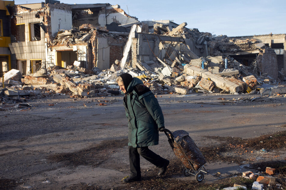 Eine ältere Dame geht mit ihrem Shopper durch eine zerstörte Ortschaft bei Bachmut.
