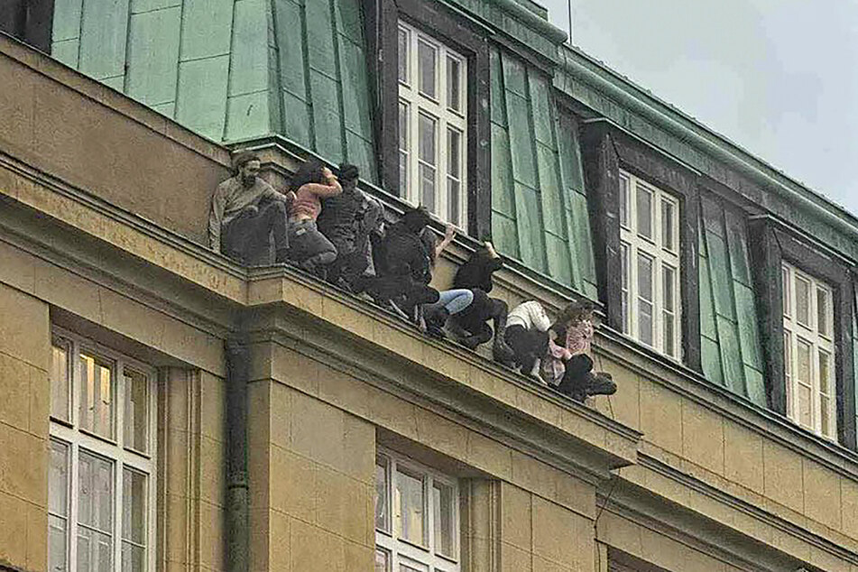 Menschen suchen Schutz unter einem Fenster der Philosophischen Fakultät der Karls-Universität. Der Killer hatte das Feuer eröffnet.