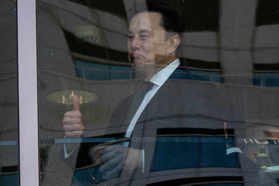 Elon Musk is seen through a window giving a "thumbs up" at the Ronald V. Dellums US Courthouse on Tuesday in Oakland, California.
