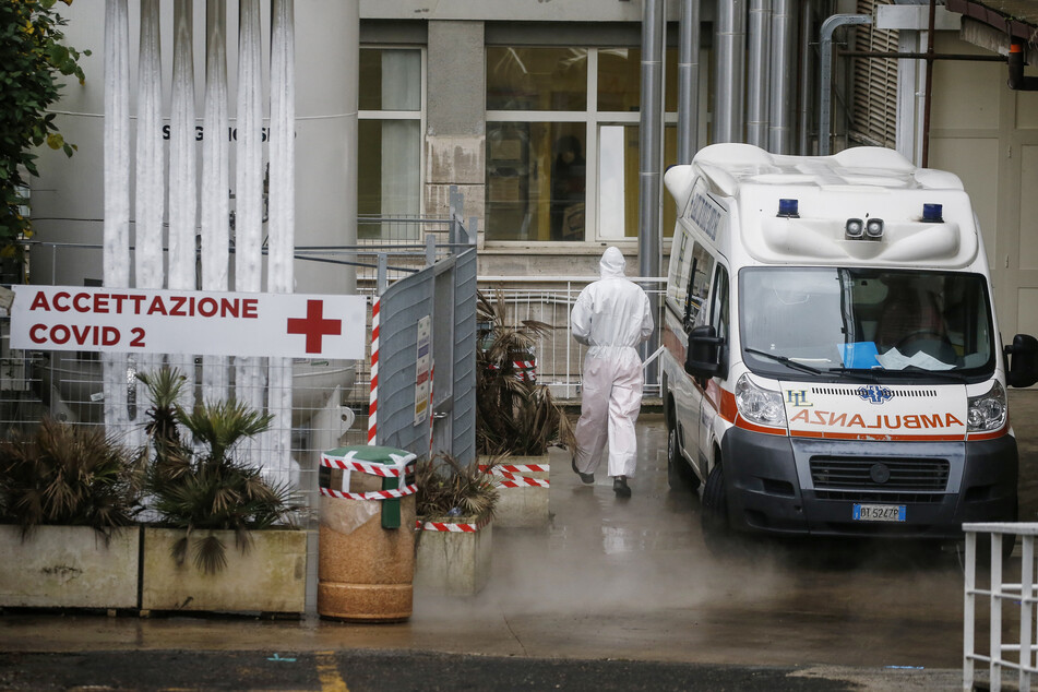 Ein medizinischer Mitarbeiter trägt einen Schutzanzug und geht neben einem Krankenwagen vorbei am Eingang des ambulantem Bereich des "Agostino Gemelli" Krankenhauses in Rom.