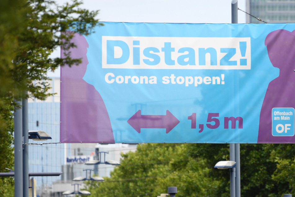 Ein großes Plakat mit der Aufschrift "Distanz! Corona stoppen!" prangt am Ortseingang von Offenbach über einer Straßenkreuzung.