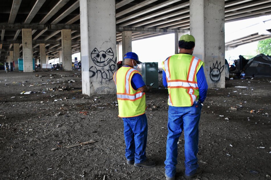 Two city workers evaluate the clean-up process under I-35 in Austin, Texas.