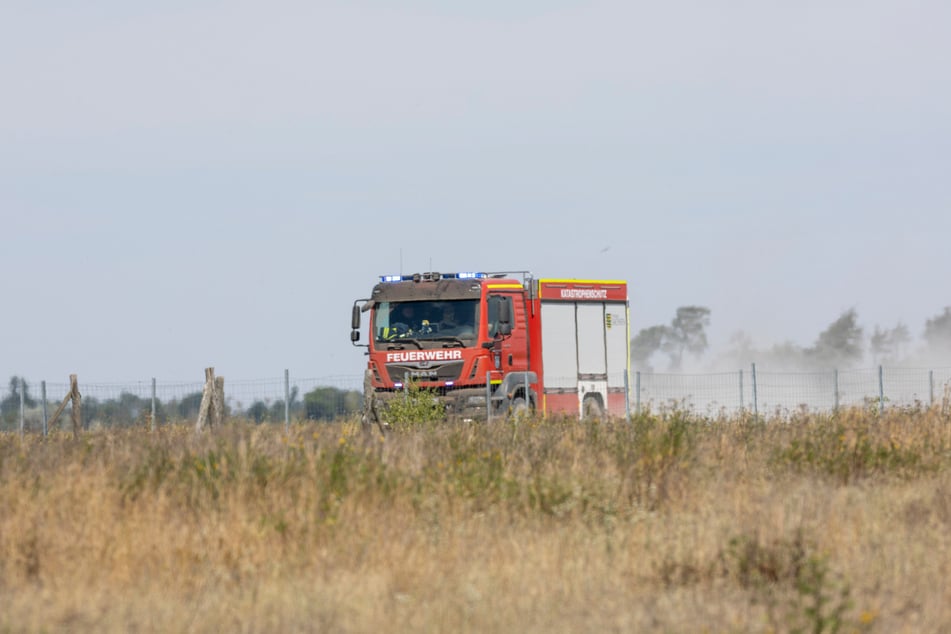Ein Feuerwehrfahrzeug ist auf staubtrockenem Boden in Richtung des Waldbrands unterwegs.