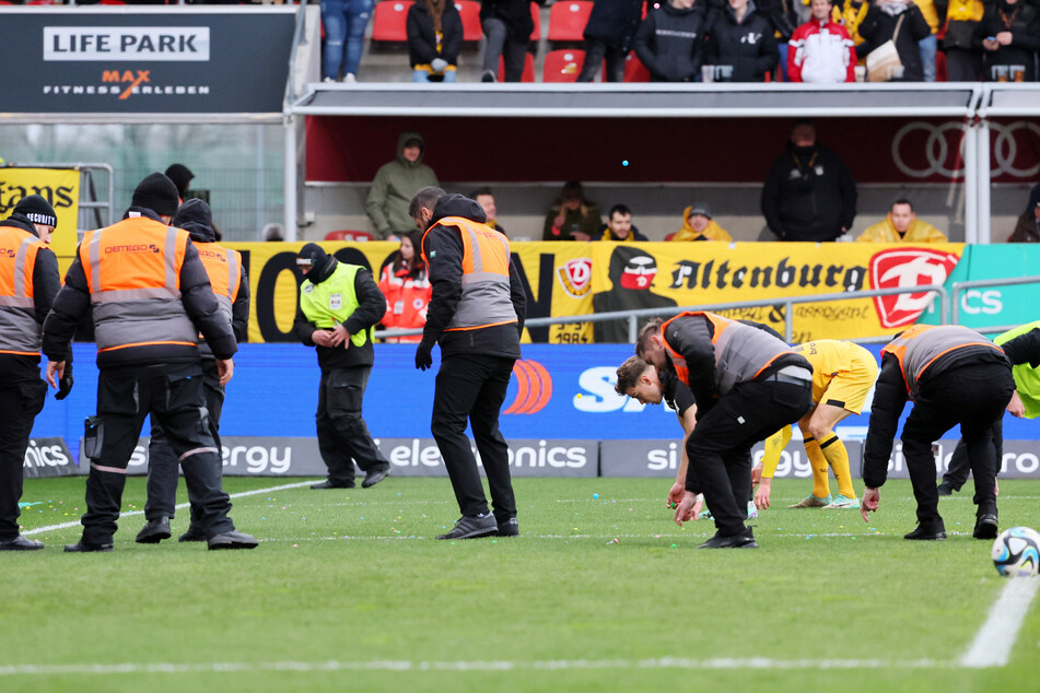 Fan-Protest beim Drittliga-Spiel zwischen Ingolstadt und Dresden: Ordner und Spieler sammeln auf das Feld geworfene Gegenstände auf.