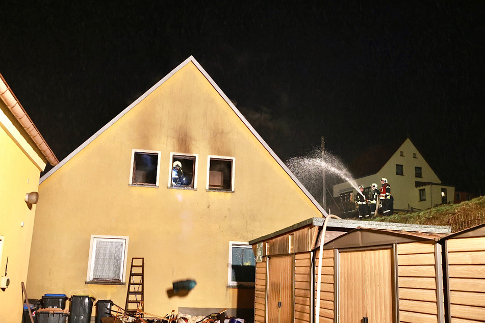 Kameraden der Feuerwehr löschen das brennende Wohnhaus.