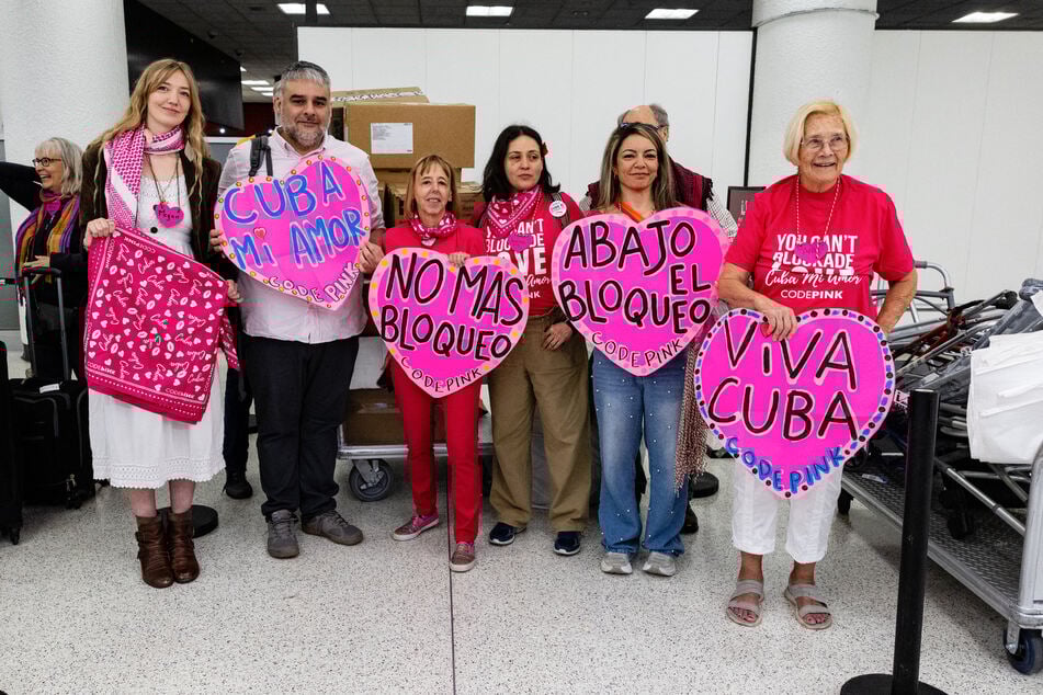 Members of the Nuestra America convoy hold signs in support of Cuba as they pose for a photo before checking in at Miami International Airport on March 20, 2026.