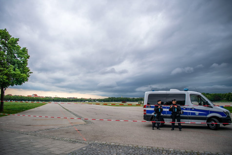 Polizisten sperren die Theresienwiese ab. Am Horizont sind Dunkle Wolken zu sehen.