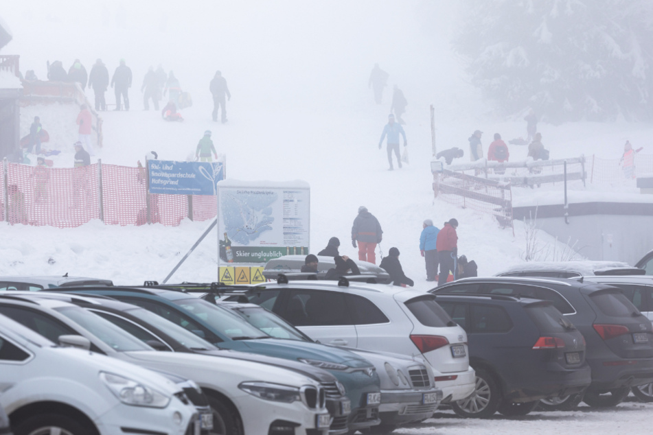 Menschen stehen am vergangenen Wochenende im dichten Nebel nahe dem Skilift am Haldenköpfle, während im Vordergrund der volle Parkplatz der geschlossenen Liftanlage zu sehen ist.