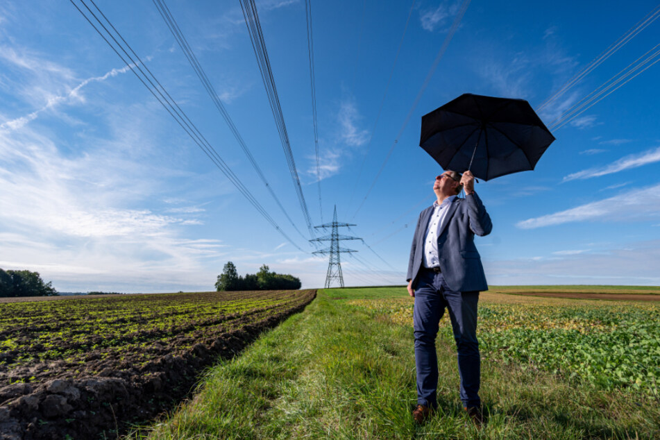 Josef Klaus, Bürgermeister von Niederaichbach, steht mit einem Regenschirm unter der problematischen Hochspannungsleitung.