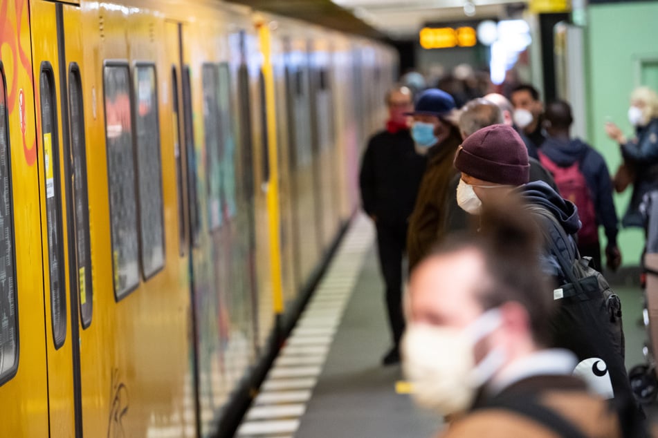 Fahrgäste mit Mund-Nasen-Schutz stehen auf dem U-Bahnhof Französische Straße in Berlin-Mitte neben der eingefahrenen U-Bahn.