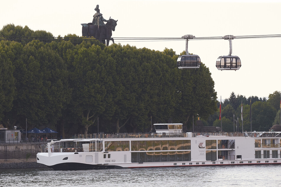 Ein Flusskreuzfahrtschiff liegt am Rheinufer in Koblenz unterhalb des Deutschen Ecks mit dem Reiterstandbild von Kaiser Wilhelm.