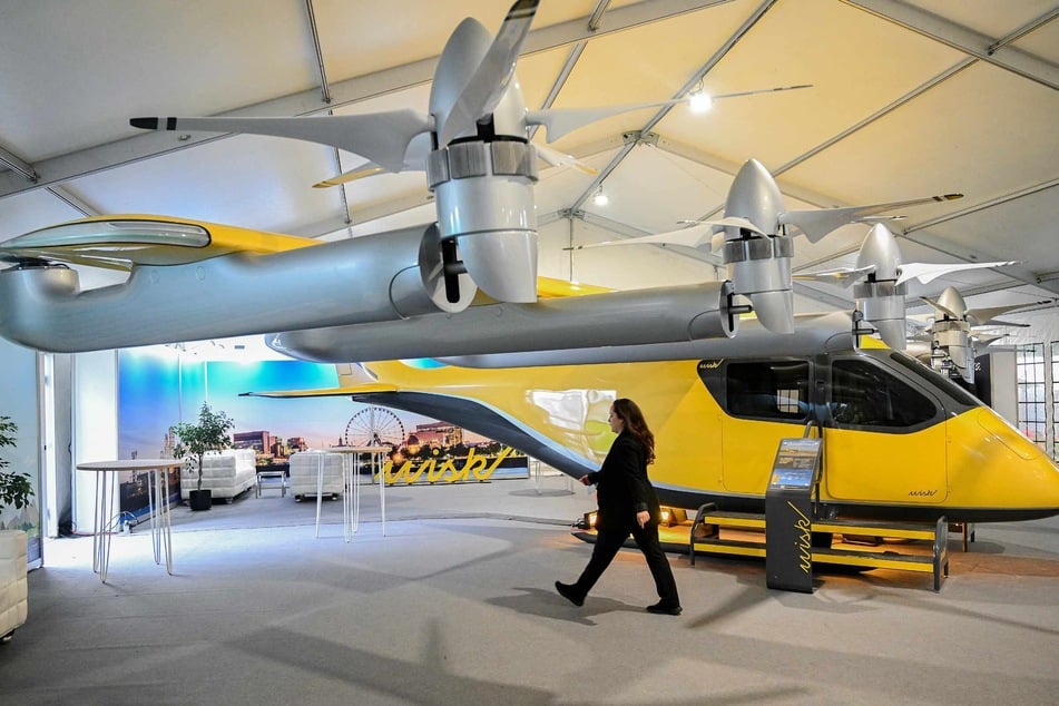 A woman walks by a Wisk self-flying all-electric four-seat air taxi during an exhibition of electric vertical take-off and landing vehicles (eVTOLs) and autonomous aircraft at the International Civil Aviation Organization's (ICAO) first Advanced Air Mobility Symposium in Montreal, Canada, September 8, 2024.