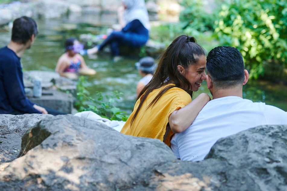 Im Viktoriapark sitzt ein Pärchen am Wasserfall während sich andere Menschen im Wasser abkühlen. Ab Dienstag erreichen die Gewitter auch Berlin.