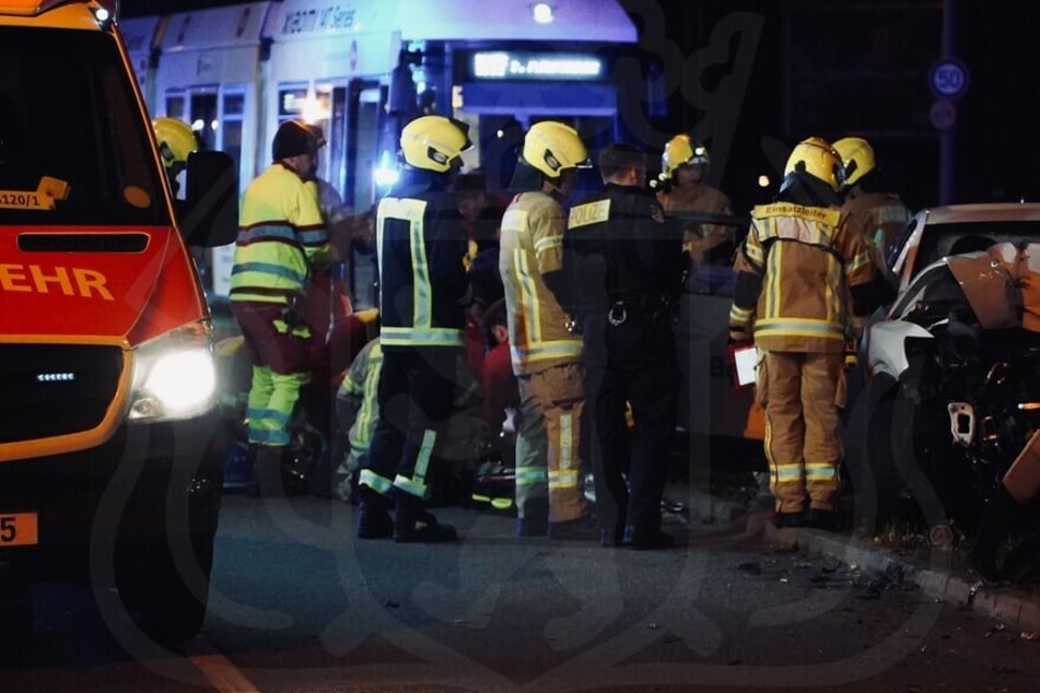 Einsatzkräfte von Feuerwehr und Polizei stehen vor dem Wrack des Mietwagens.