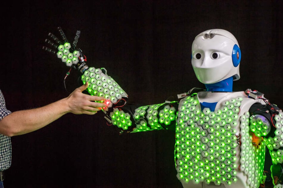 Der Arm eines Wissenschaftlers berührt einen humanoiden Roboter.