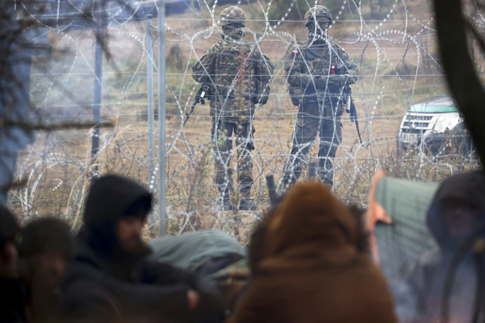 Polnische Grenzschützer stehen hinter Stacheldraht Wache, hinter harren Migranten der belarussisch-polnischen Grenze aus.