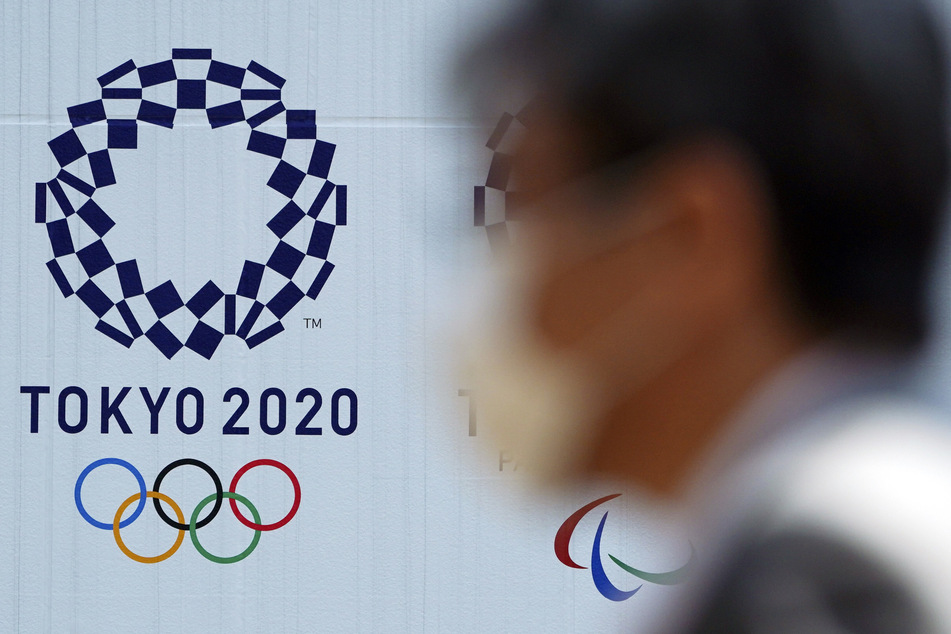 Ein Mann geht mit einem Mundschutz an einem Plakat vorbei, mit dem für die Olympischen Spiele 2020 in Tokio geworben wird.