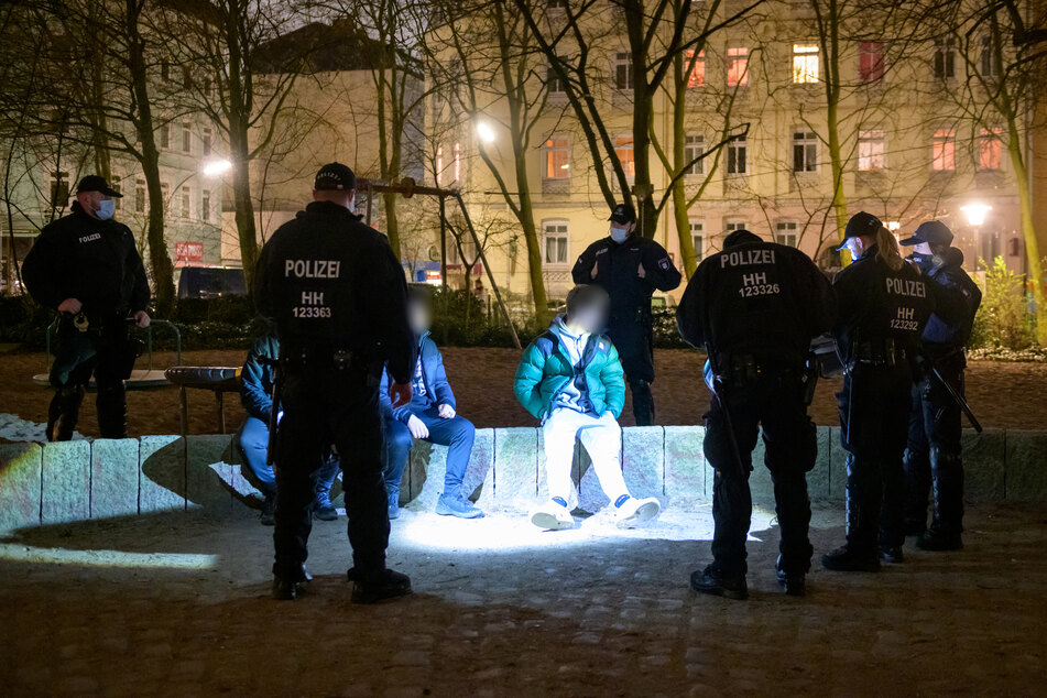 Drei junge Männer werden von Bereitschaftspolizisten auf einem Spielplatz kontrolliert. In Hamburg treten ab Karfreitag zur Bekämpfung der Corona-Pandemie nächtliche Ausgangsbeschränkungen in Kraft.