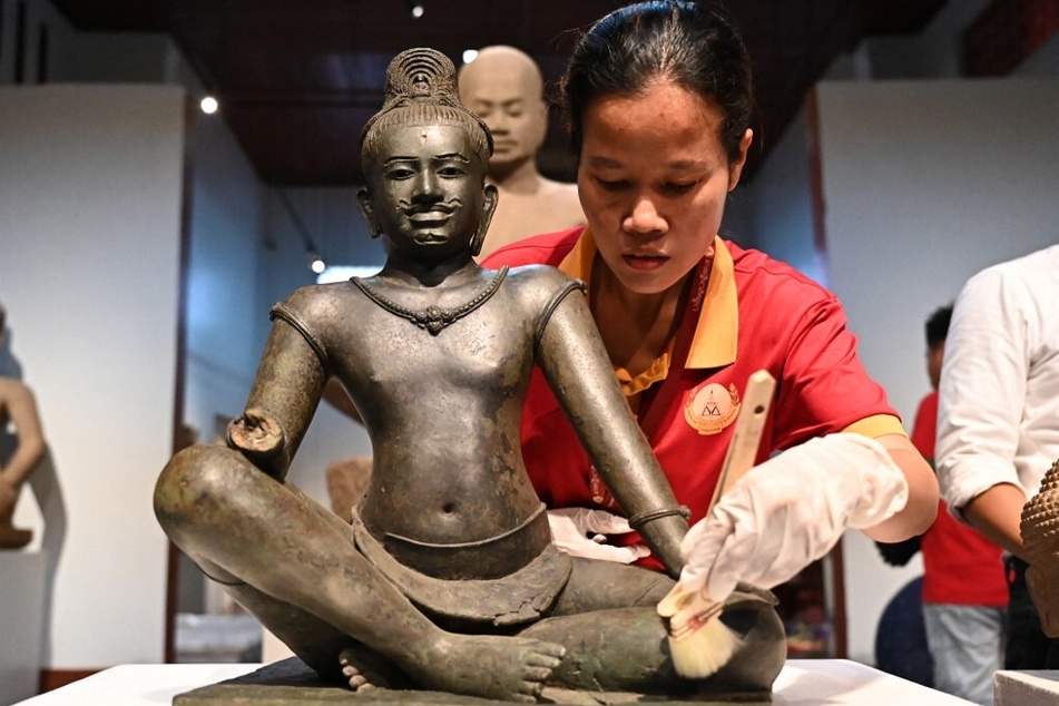 A worker cleans Budhisattva Avalokiteshvara, a copper alloy sculpture with silver inlay from the 10th-early 11th century Angkor period, during a repatriation event.