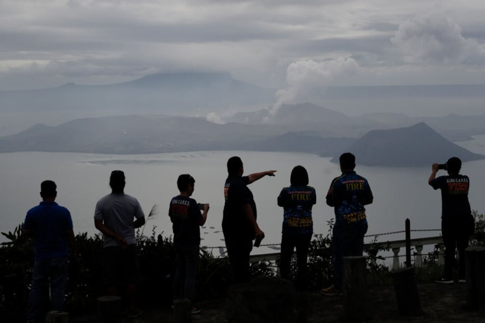Leute schauen auf den Vulkan "Taal" in Tagaytay, aus dem eine Wolke aufsteigt.