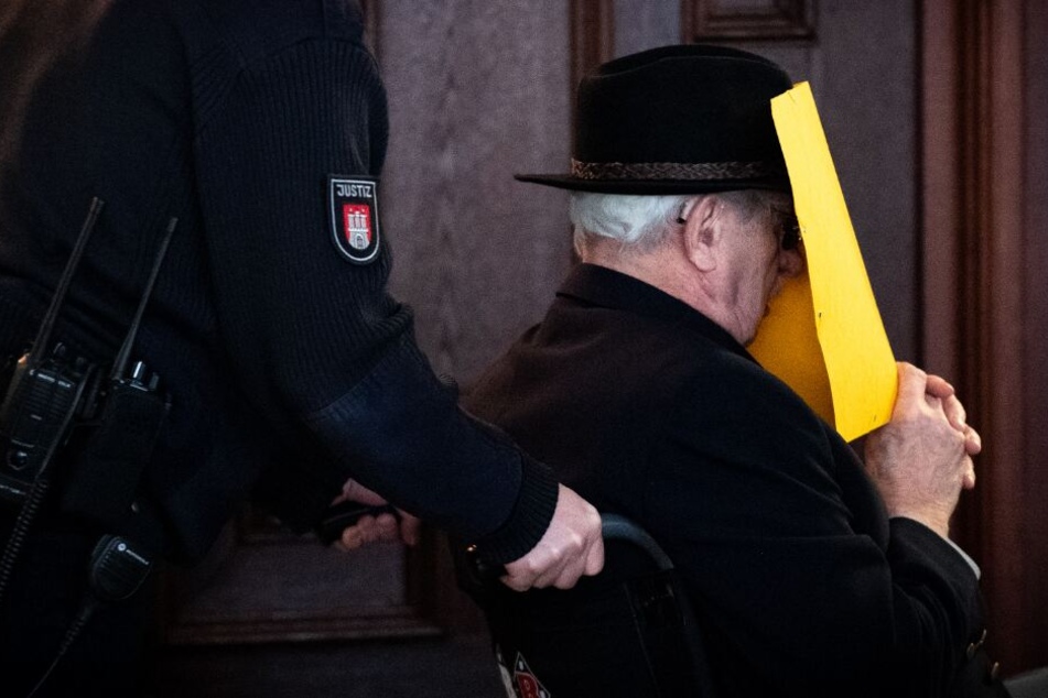 Der Angeklagte wird in einer Pause in einem Rollstuhl aus dem Gerichtssaal gebracht.