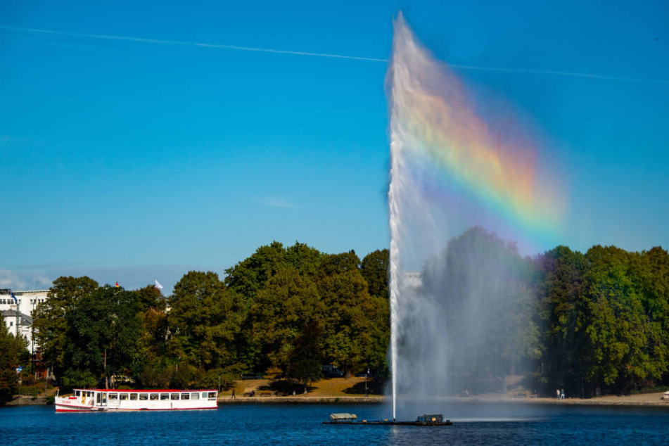 Ein Regenbogen entsteht durch die Sonnenstrahlen in der Alsterfontäne, die gerade von einem Alsterausflugsdampfer passiert wird.