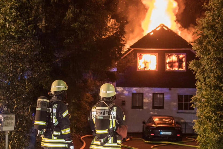 Feuerwehrleute stehen vor dem brennenden Haus.