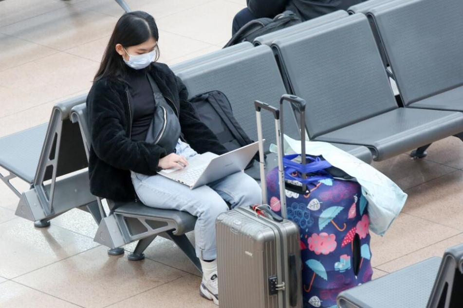 Ein junge Frau aus Indonesien sitzt mit einem Mundschutz in einer Abfertigungshalle im Flughafen Hamburg.