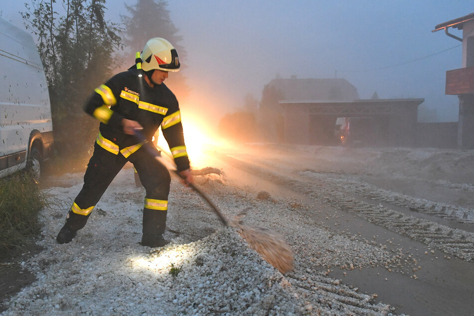 Feuerwehrleute räumen Hagel zur Seite. In Österreich haben Unwetter mit großen Hagelkörnern zahlreiche Gebäude und Autos beschädigt.