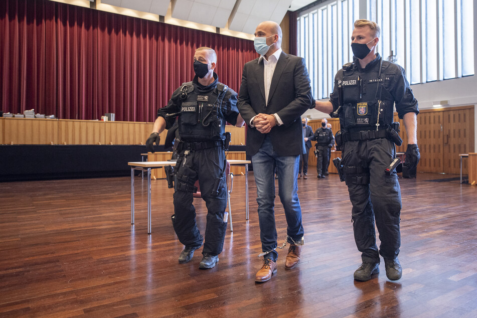 An Händen und Füßen gefesselt ist einer der Hauptangeklagten, den bewaffnete Polizisten in die zu einem Gerichtssaal umfunktionierte Kongresshalle in Gießen bringen.