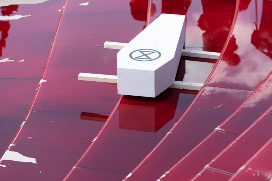 Die Klimaschützer haben einen Sarg mit dem Symbol der Gruppierung Extinction Rebellion einer blutroten Flüssigkeit am Hamburger Hafen abgestellt.