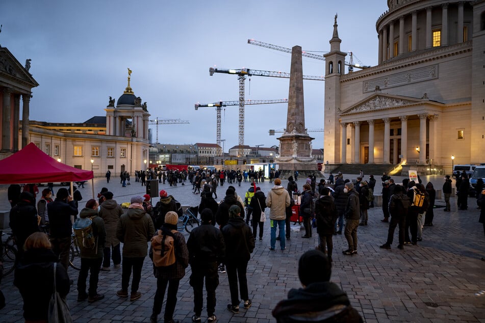 Gegendemonstranten (vorne) stehen neben der Protestaktion des AfD-Kreisverbandes Potsdam gegen die 2G-/3G-Regeln und eine eventuelle Corona-Impfpflicht vor der St. Nikolaikirche.