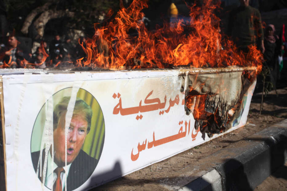 Palästinensische Autonomiegebiete, Gaza: Während eines Protestes am Freitag von Unterstützern der Hamas gegen die USA brennt ein Plakat mit Bildern des US-Präsidenten Trump und des israelischen Premierministers Netanjahu auf einem Holzkasten.