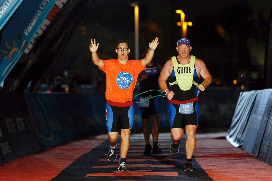 Mit hochgestreckten Armen läuft Chris Nikoc (l) neben seinem Trainer Dan Grieb beim Ironman 2020 über die Ziellinie.