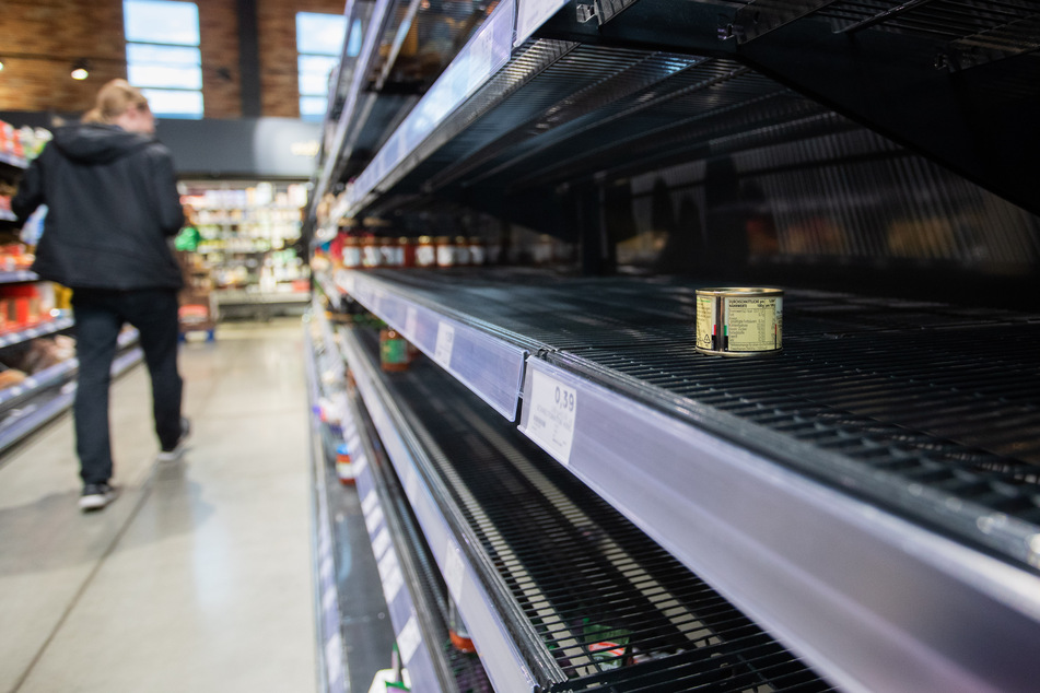 Ein Kunde des Supermarkts läuft an einem leeren Regal vorbei, in dem eine Dose liegt.