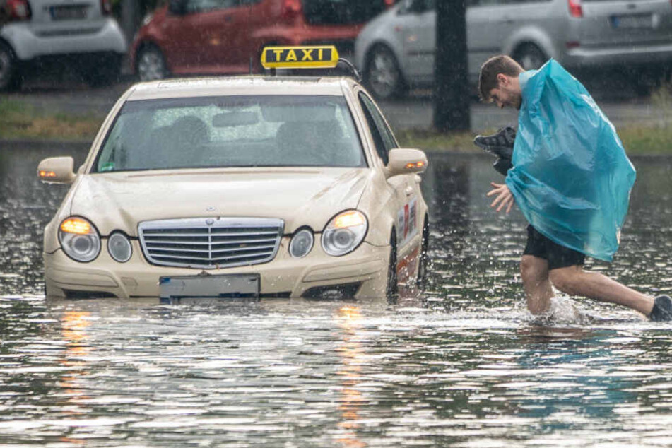 Ein Fußgänger und ein Taxi kämpfen sich durch die Regenmassen.