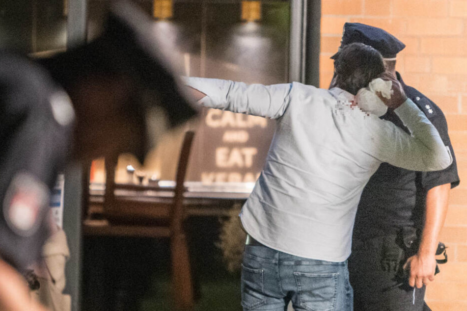 Ein Beteiligter kühlt sich seine blutende Wunde mit Eis, während er mit einem Polizisten spricht.