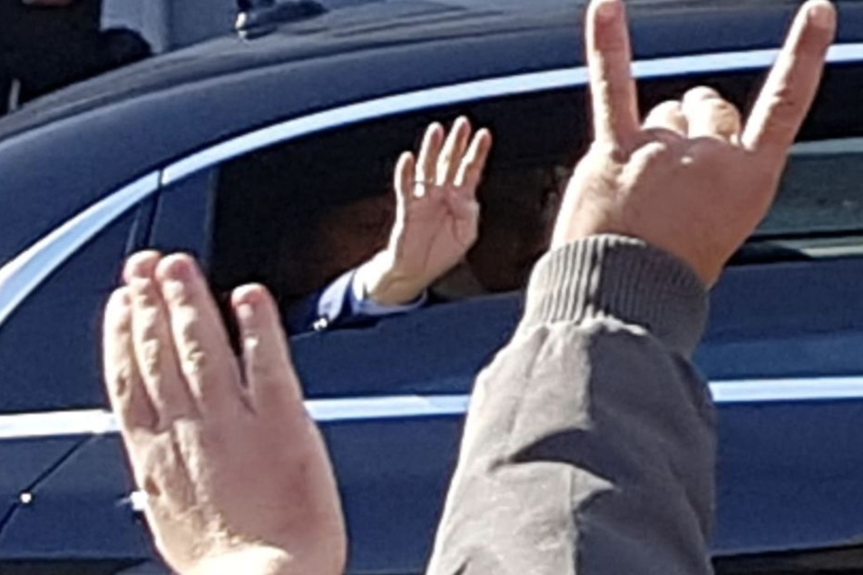 Einige grüßen Erdogan mit dem "Wolfsgruß" zurück, dem Zeichen der türkischen Rechtsextremisten (zwei Finger hoch, die anderen zu einer Schnauze geformt).